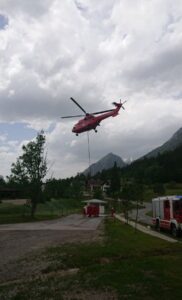 Hubschrauber beim Betanken des Wasserbehälters während Löscharbeiten eines Waldbrandes