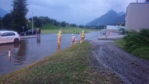 Drei Feuerwehrmitglieder beim reinigen eines Oberflächenschachtes an der Landesstraße nach ergiebigen Regengüssen